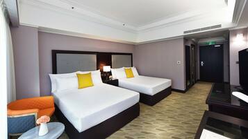 A hotel room with two beds, a small table with a vase, an orange chair, and a TV.