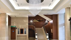 En hotellobby med en stor lysekrone, en trappe og en receptionsdisk.