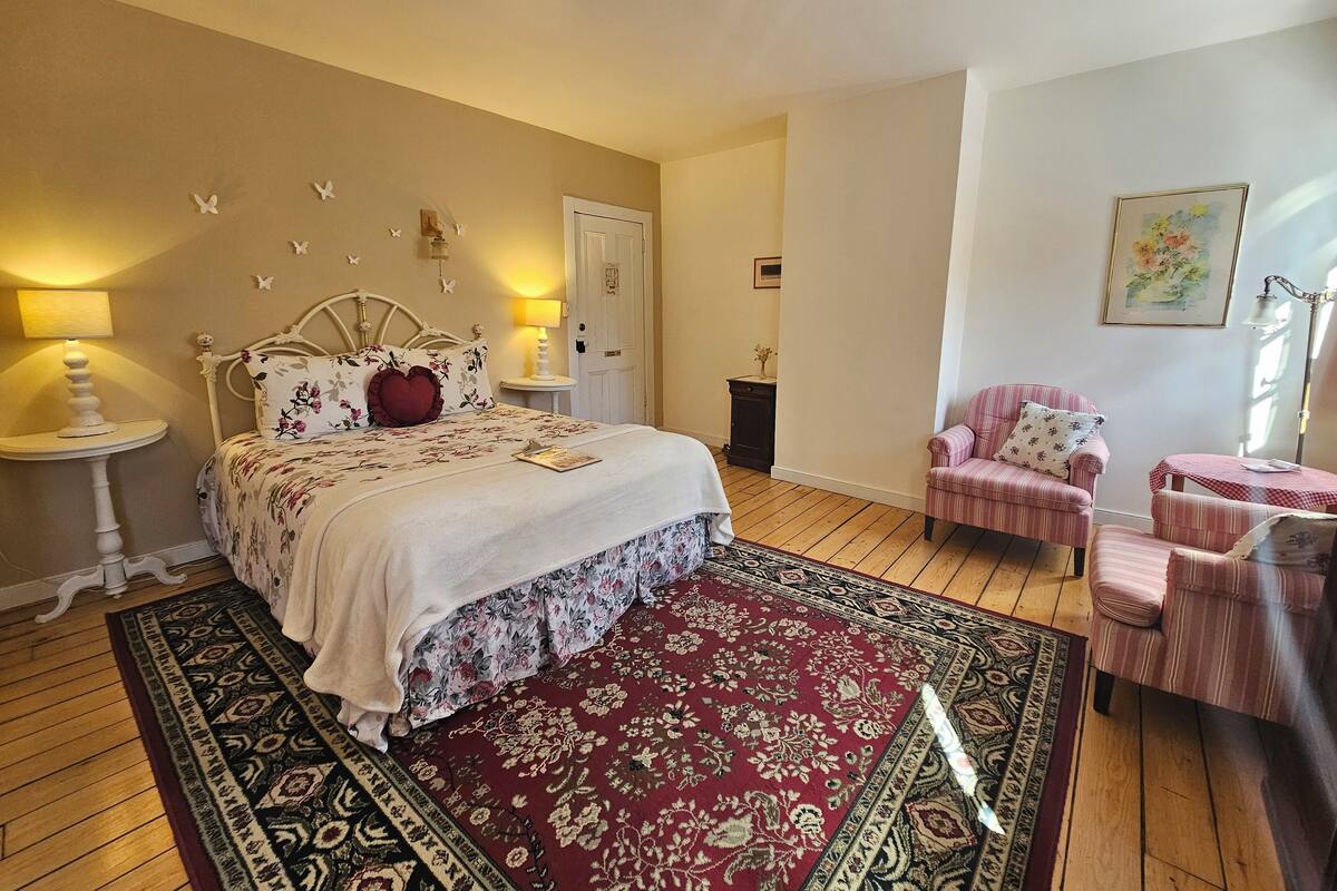 A bedroom with a bed, bedside tables, a chair, a small table, and a rug.