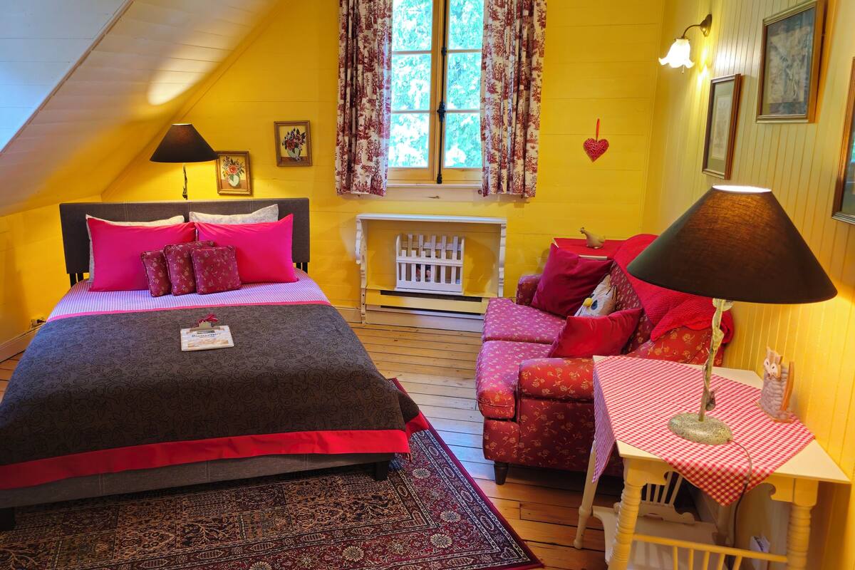 A bedroom with a bed, a small table, a chair, and a window with curtains.