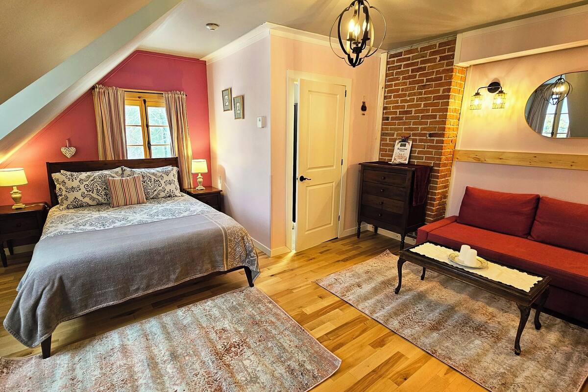 A bedroom with a bed, a red sofa, a dresser, a mirror, and a chandelier.