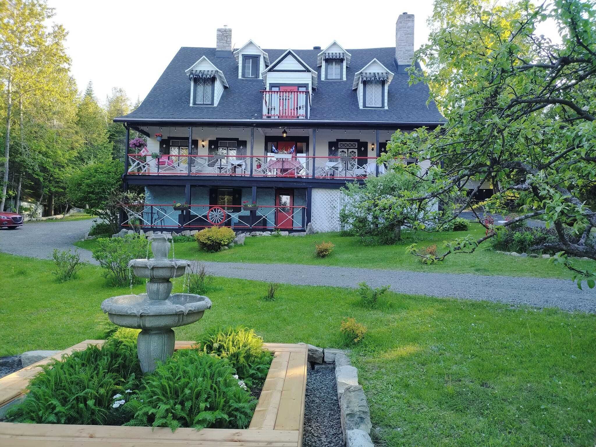 Un edificio de dos plantas con balcón, una fuente de piedra y un jardín bien cuidado.