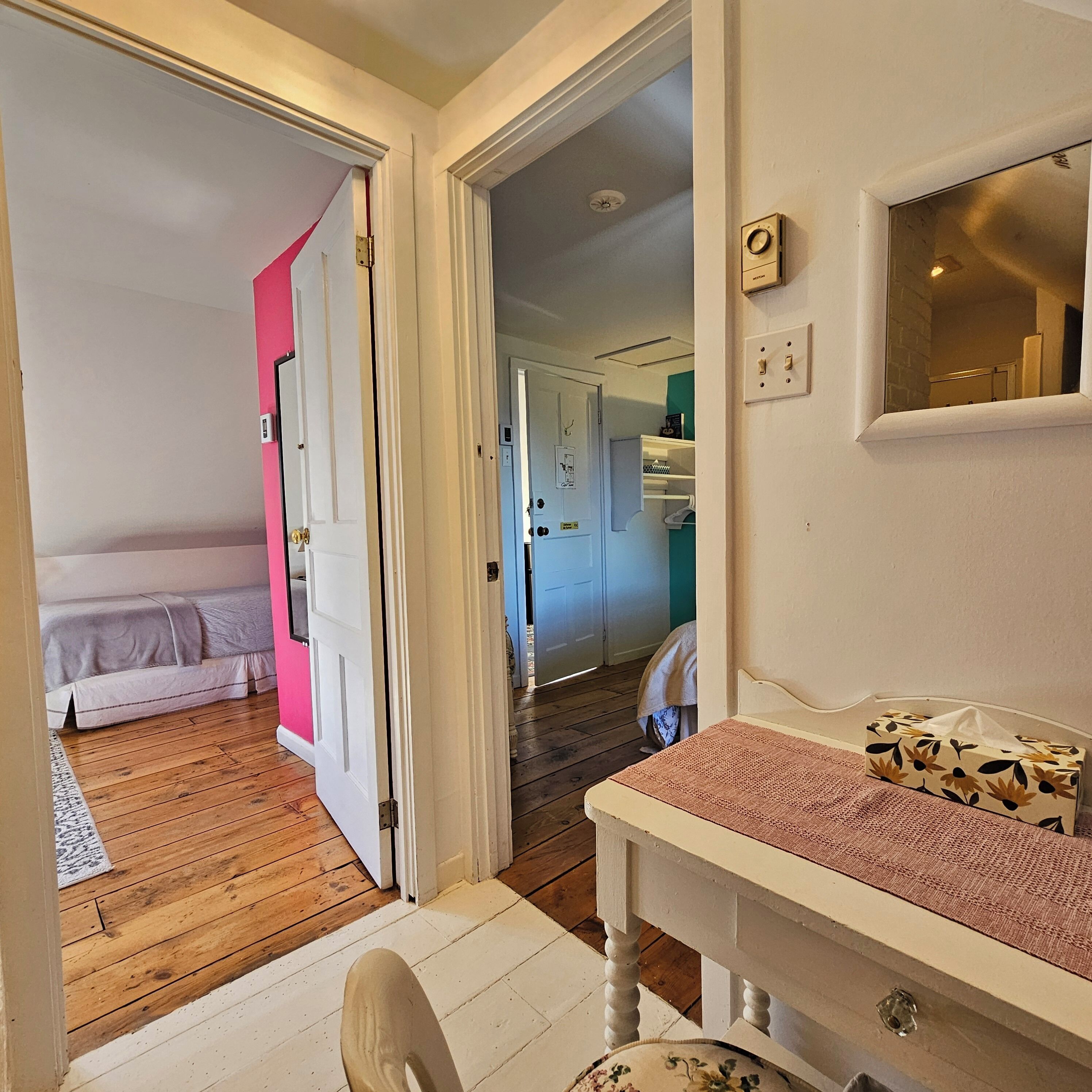 Un pasillo con piso de madera que conduce a un dormitorio con cama y puerta rosa.