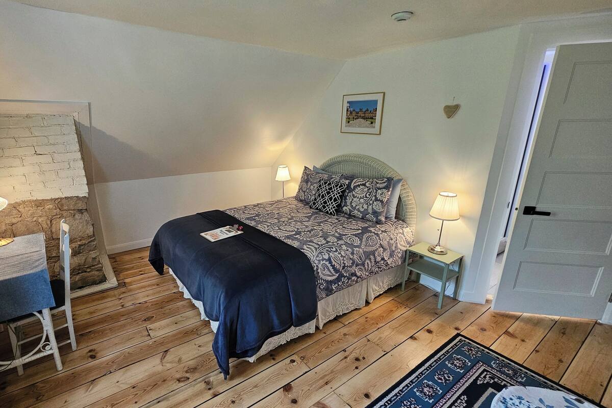 A bedroom with a bed, bedside lamps, a wooden floor, a small table, and a door.