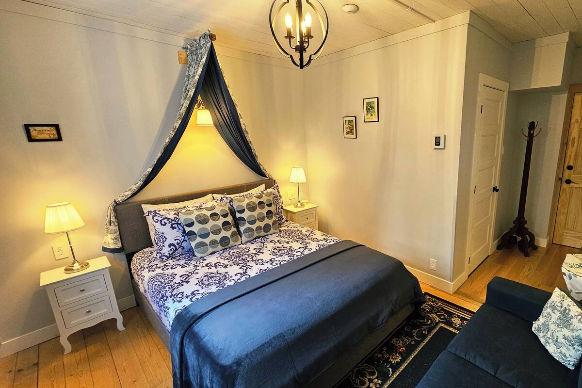 A bedroom with a bed, nightstands, a lamp, a guitar, and a door.