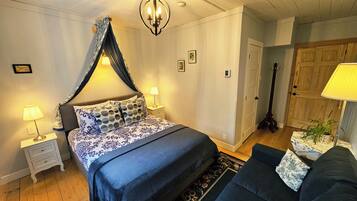 A bedroom with a bed, nightstands, a lamp, a guitar, and a door.