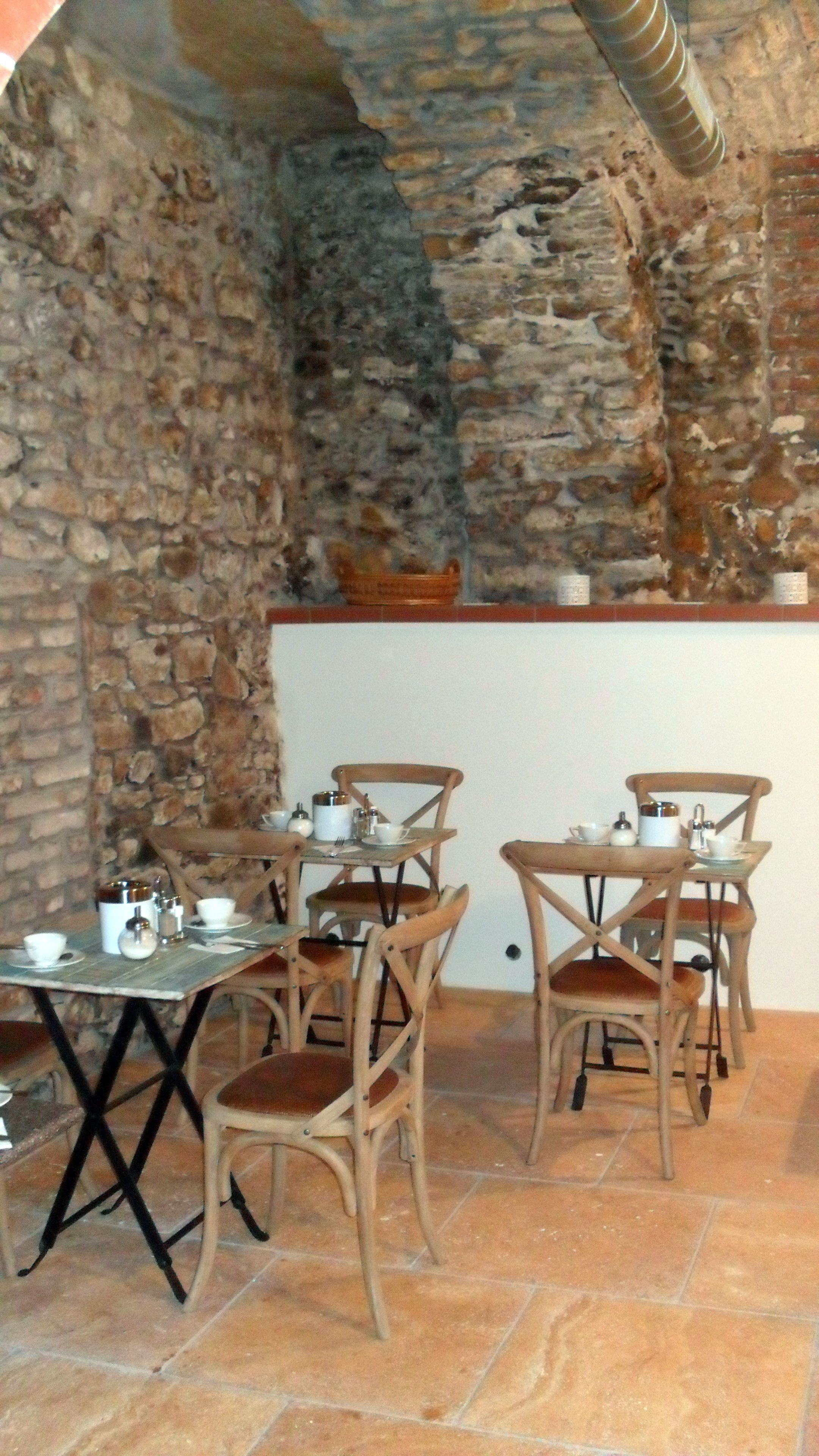 A rustic dining area with stone walls, wooden chairs, and a table set with tea pots and cups.