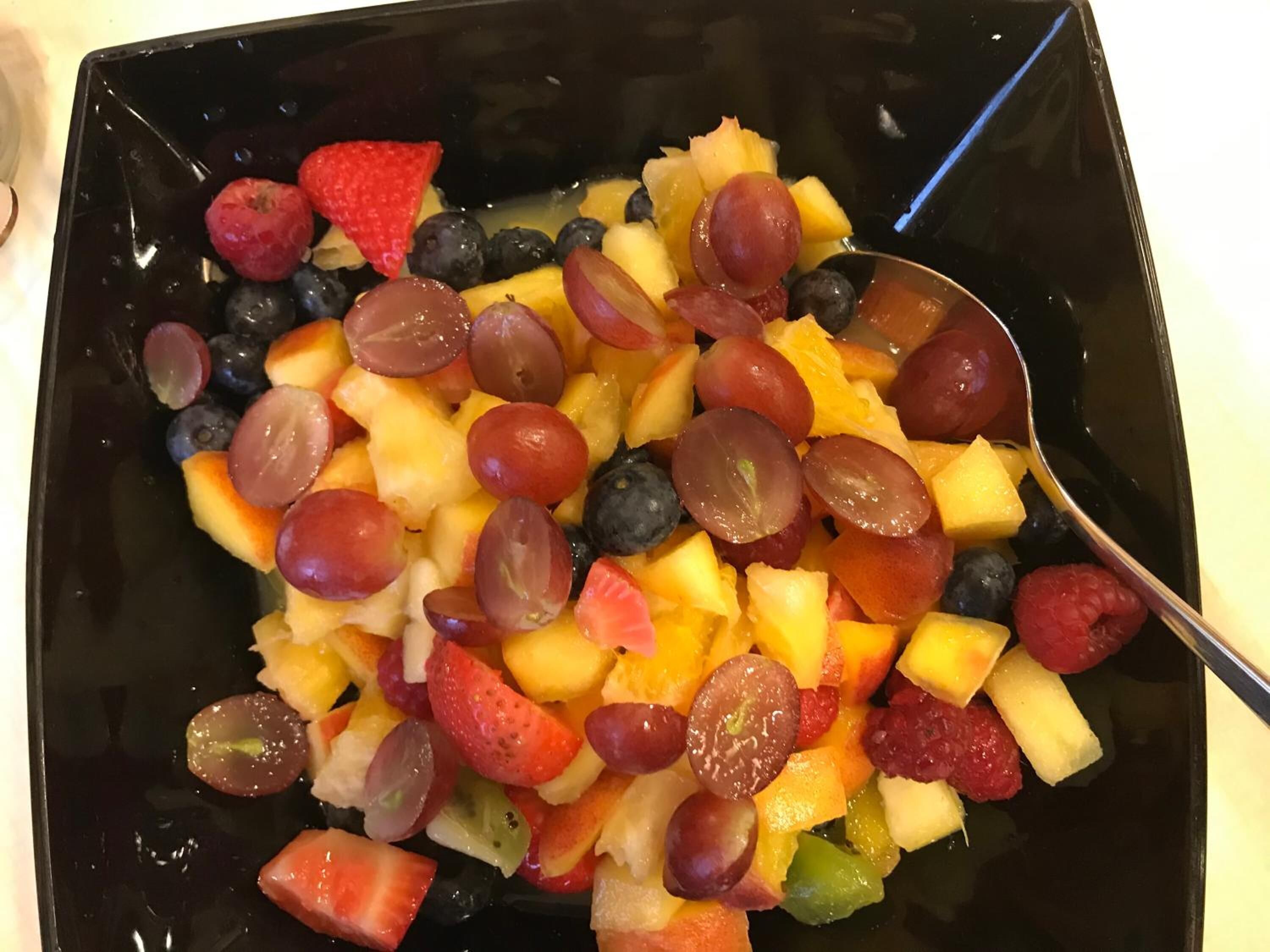 Un tazón negro lleno de frutas variadas como uvas, fresas y trozos de piña.