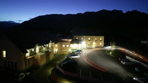 Un hotel con una entrada en curva, varios coches estacionados y montañas al fondo.