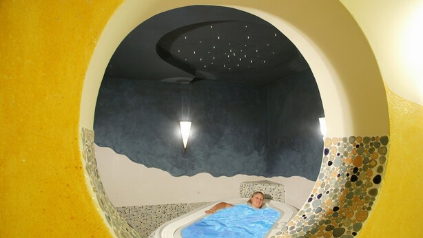 Una habitación circular con una cama en el centro, una lámpara en el techo y una pared con textura.