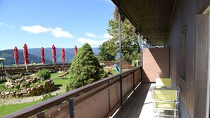 Un balcón con vistas a montañas, una cerca de madera y una mesa con sillas.