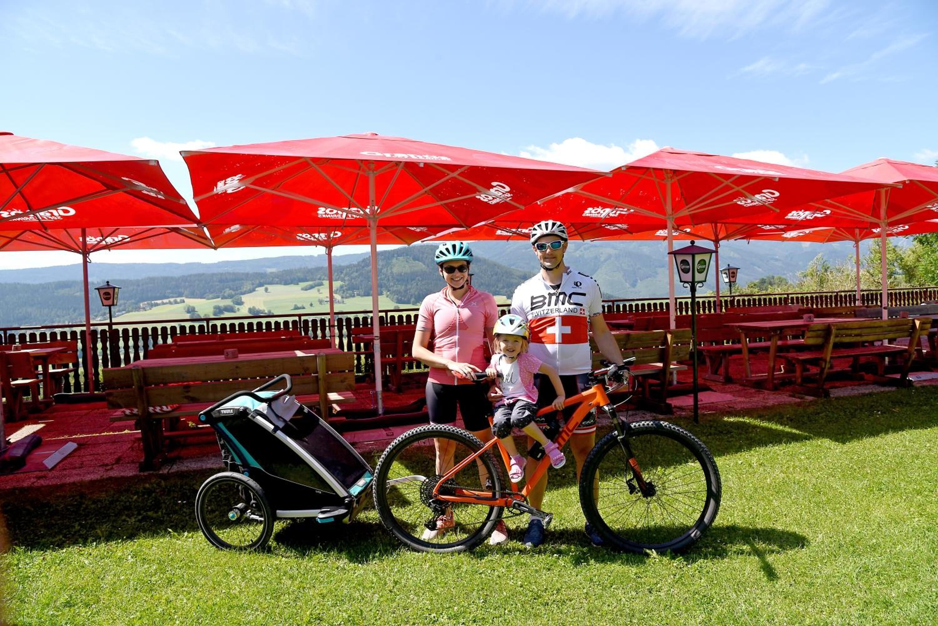 A terrace with red umbrellas, a stroller, and bicycles.