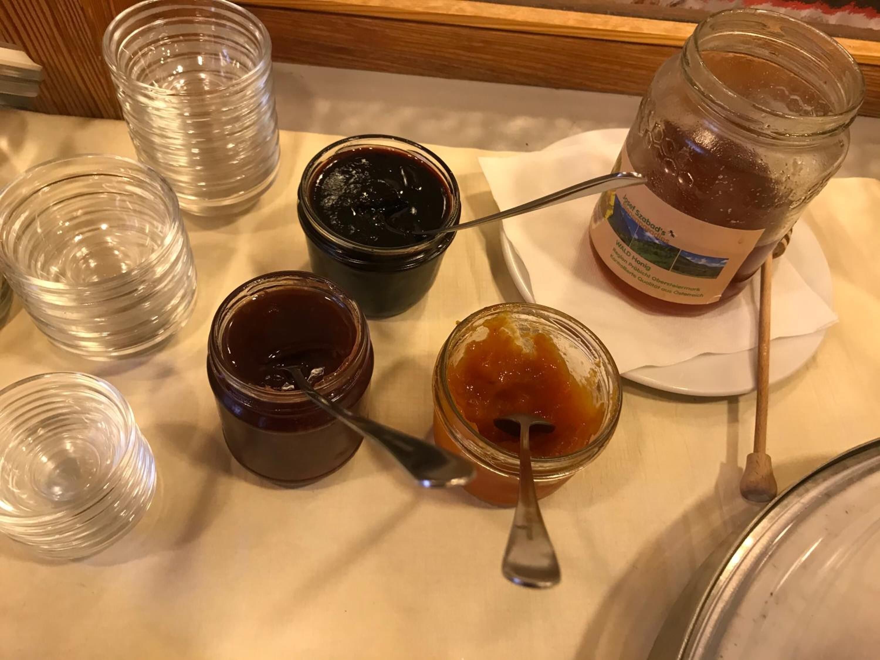 A table with various jars of jam and a bottle of jam on a white tablecloth.