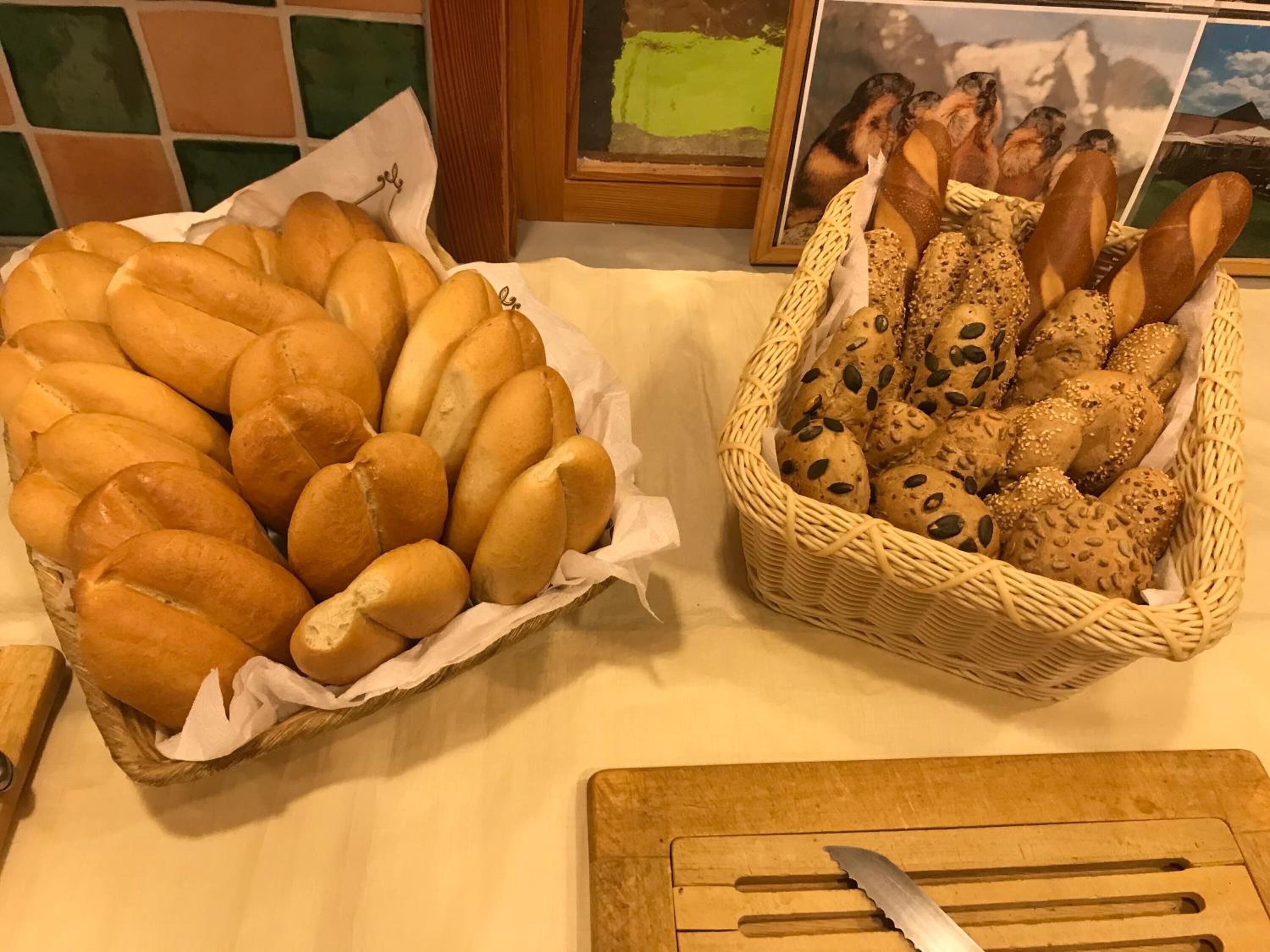 Two baskets of bread on a table with a wooden cutting board and a knife.