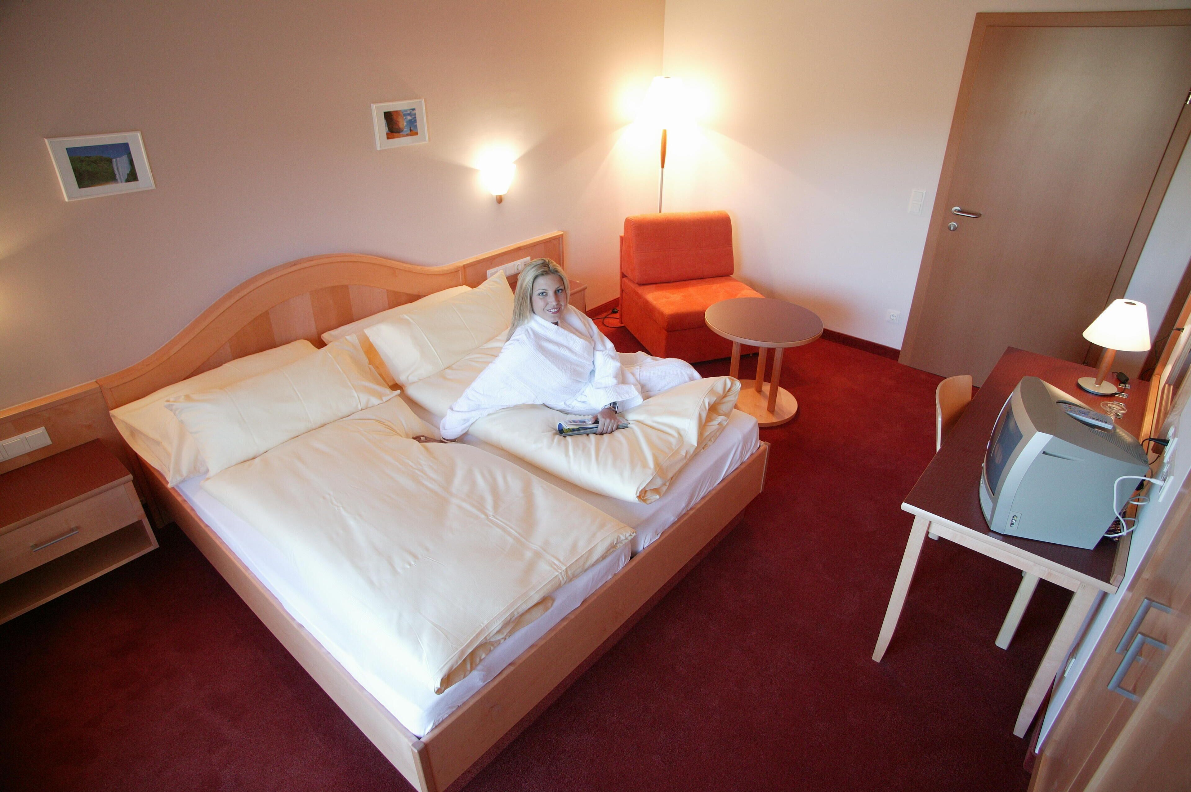 Habitación de hotel con cama, una silla, una mesita y televisor.