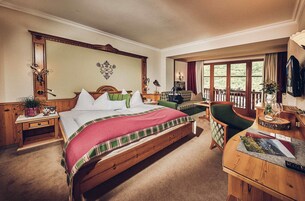Un dormitorio amplio con una cama grande, un escritorio de madera, una silla y un balcón con vistas al exterior.