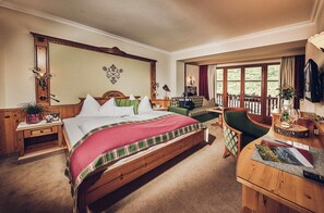 A spacious bedroom with a large bed, a wooden desk, a chair, and a balcony with a view of the outdoors.