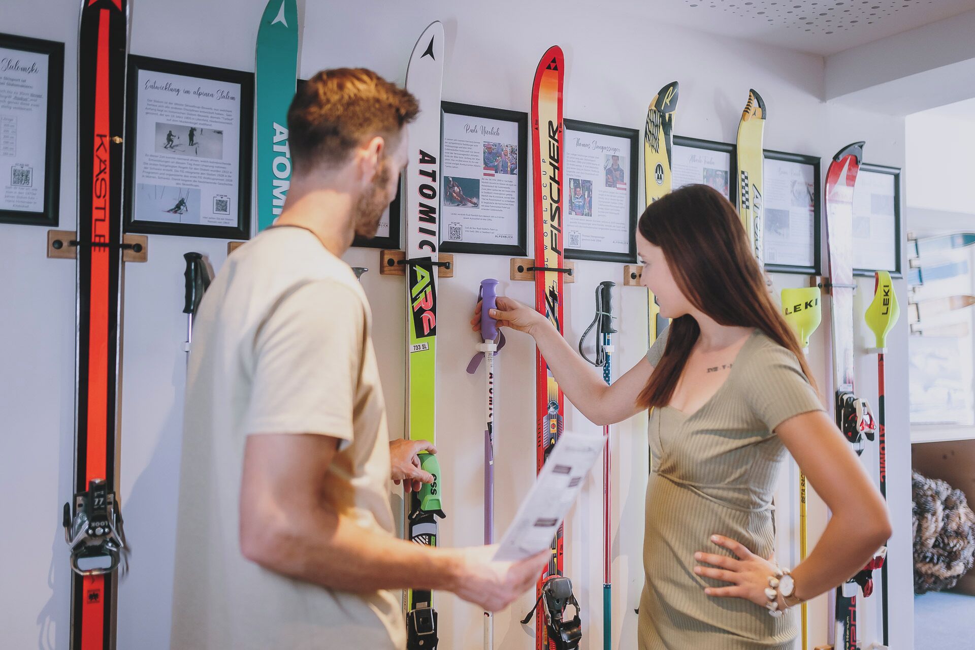 A ski shop with various skis displayed on the wall and a customer and a shop assistant examining a ski.