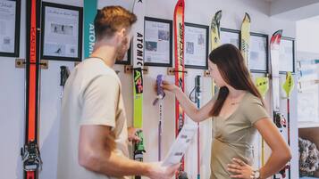 A ski shop with various skis displayed on the wall and a customer and a shop assistant examining a ski.