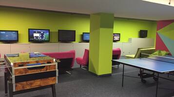 A room with a foosball table, several chairs, and multiple screens on the wall.