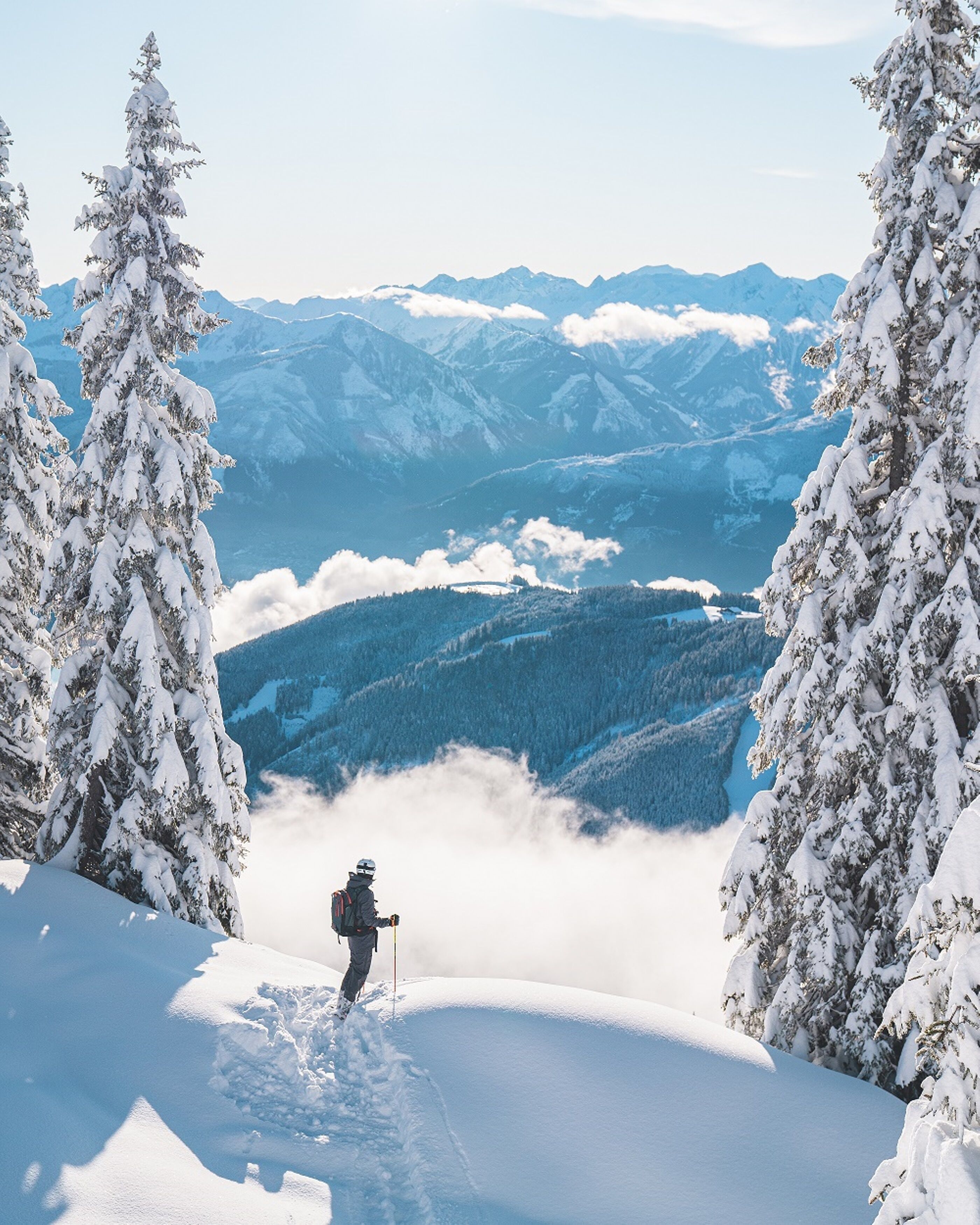 Un paysage de montagne enneigé, avec un randonneur au premier plan et une vue sur des montagnes et des vallées lointaines.