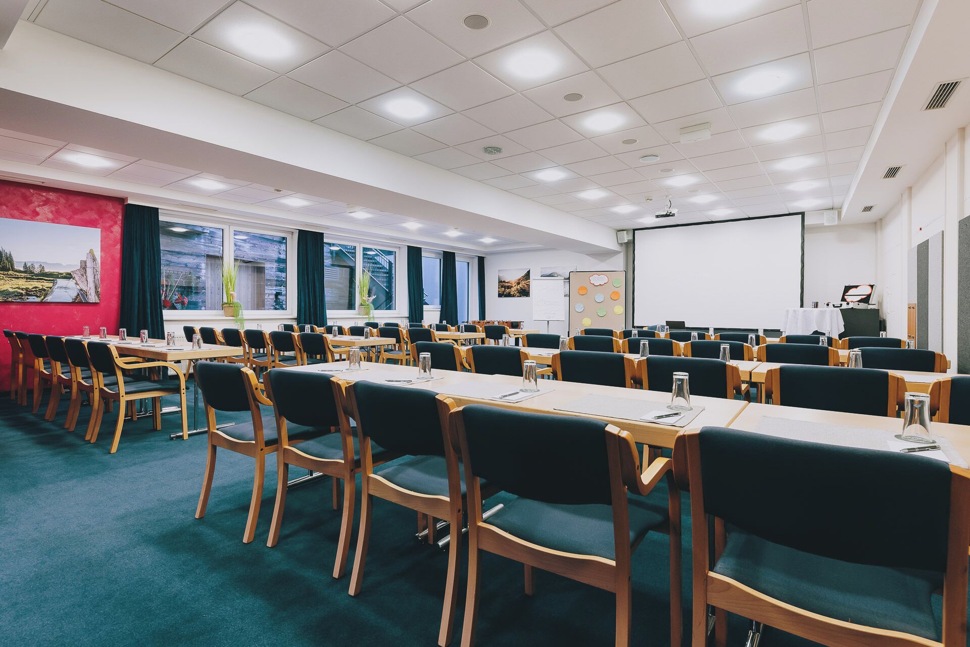 Un salón de conferencias con varias mesas y sillas, una pizarra y una pantalla para proyector.