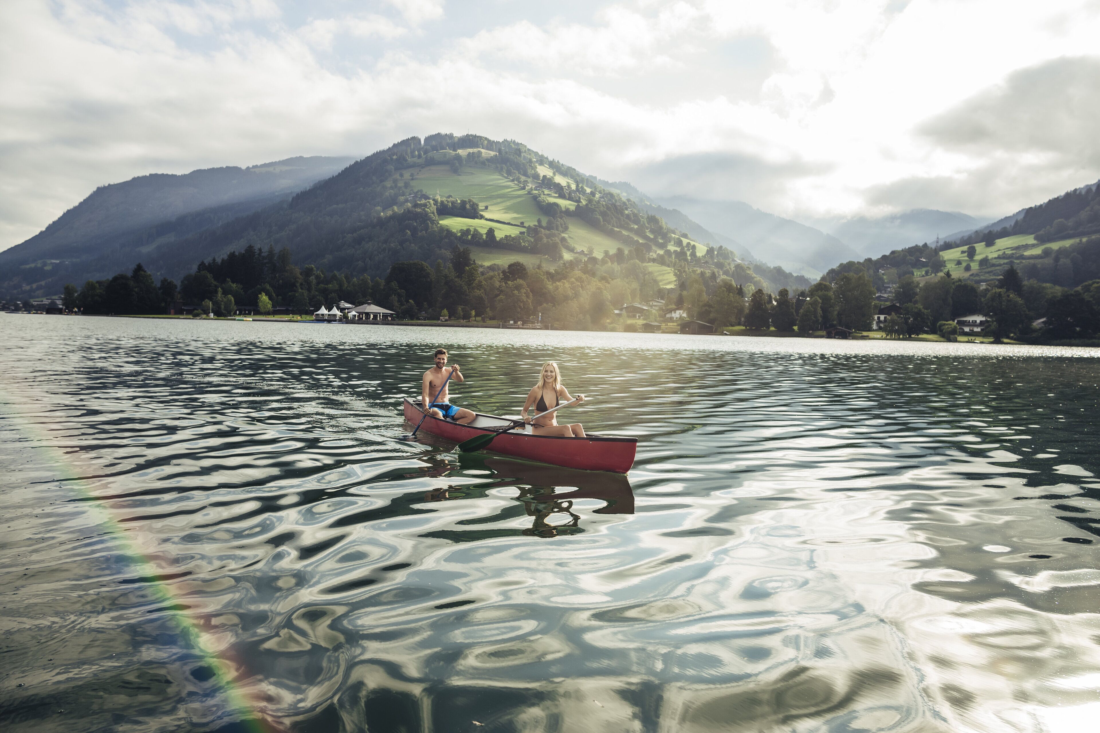 A calm lake with two people in a red canoe, surrounded by mountains and clear skies.
