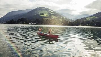 A calm lake with two people in a red canoe, surrounded by mountains and clear skies.