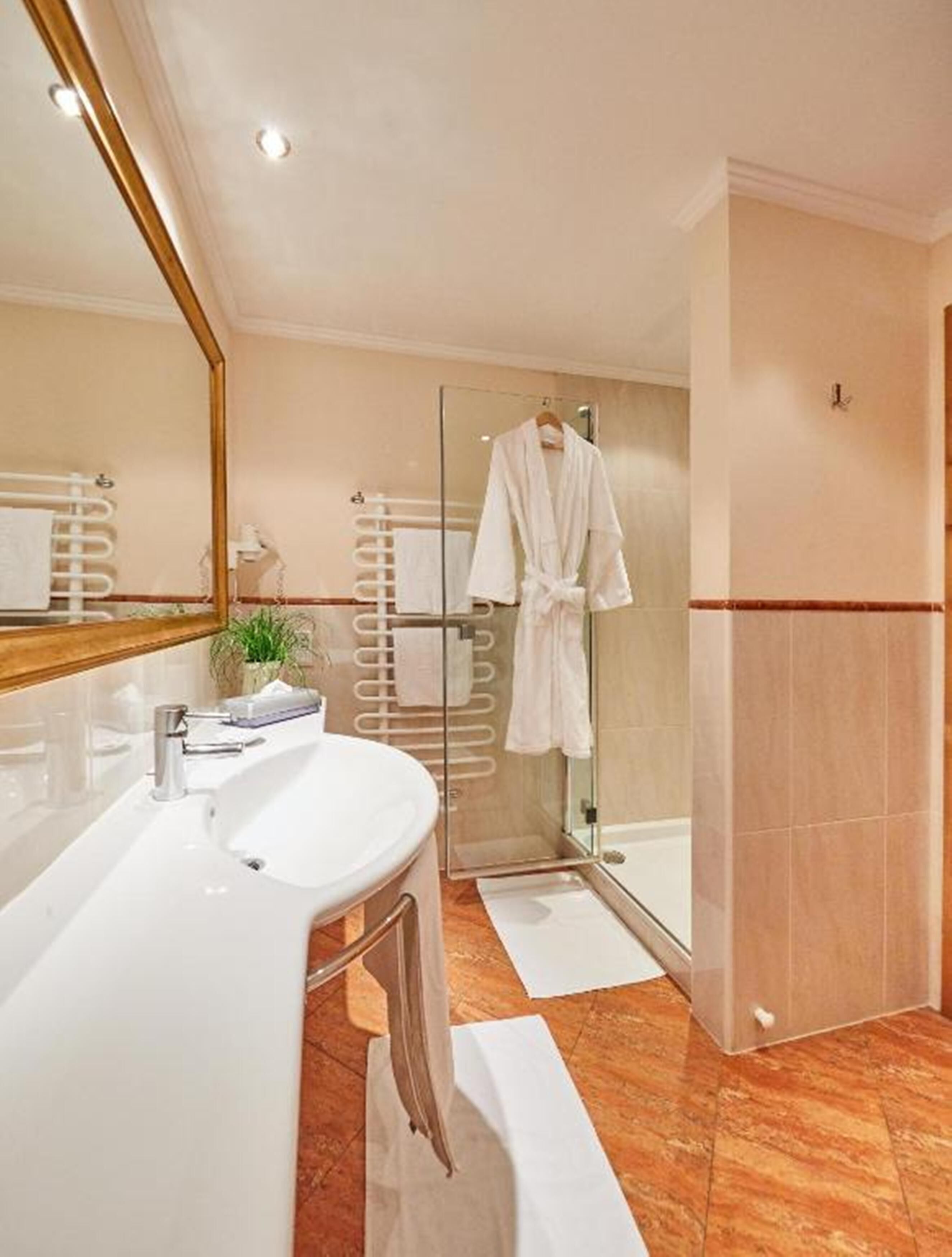 A modern bathroom with a white sink, a glass shower enclosure, and a white bathrobe hanging on a rack.