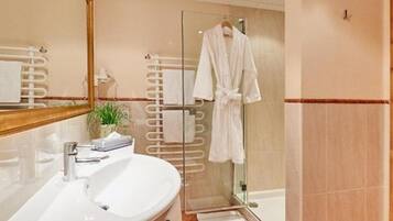 A modern bathroom with a white sink, a glass shower enclosure, and a white bathrobe hanging on a rack.