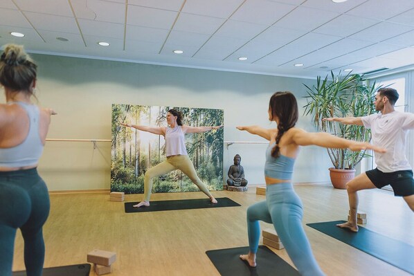 Una clase de yoga en una habitación con suelo de madera, un ventanal grande y una estatua de Buda.