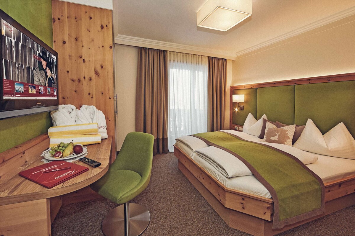 A hotel room with a bed, a desk with a computer, a chair, and a television.