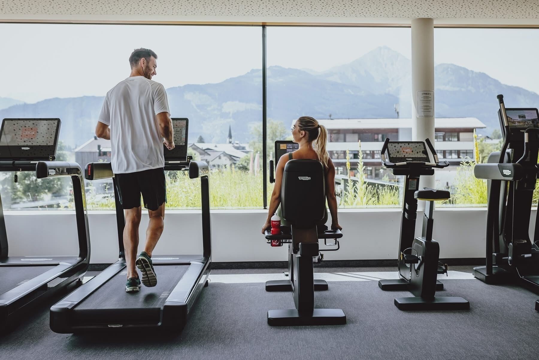 A gym with treadmills and exercise equipment, large windows with a mountain view, and a modern interior design.