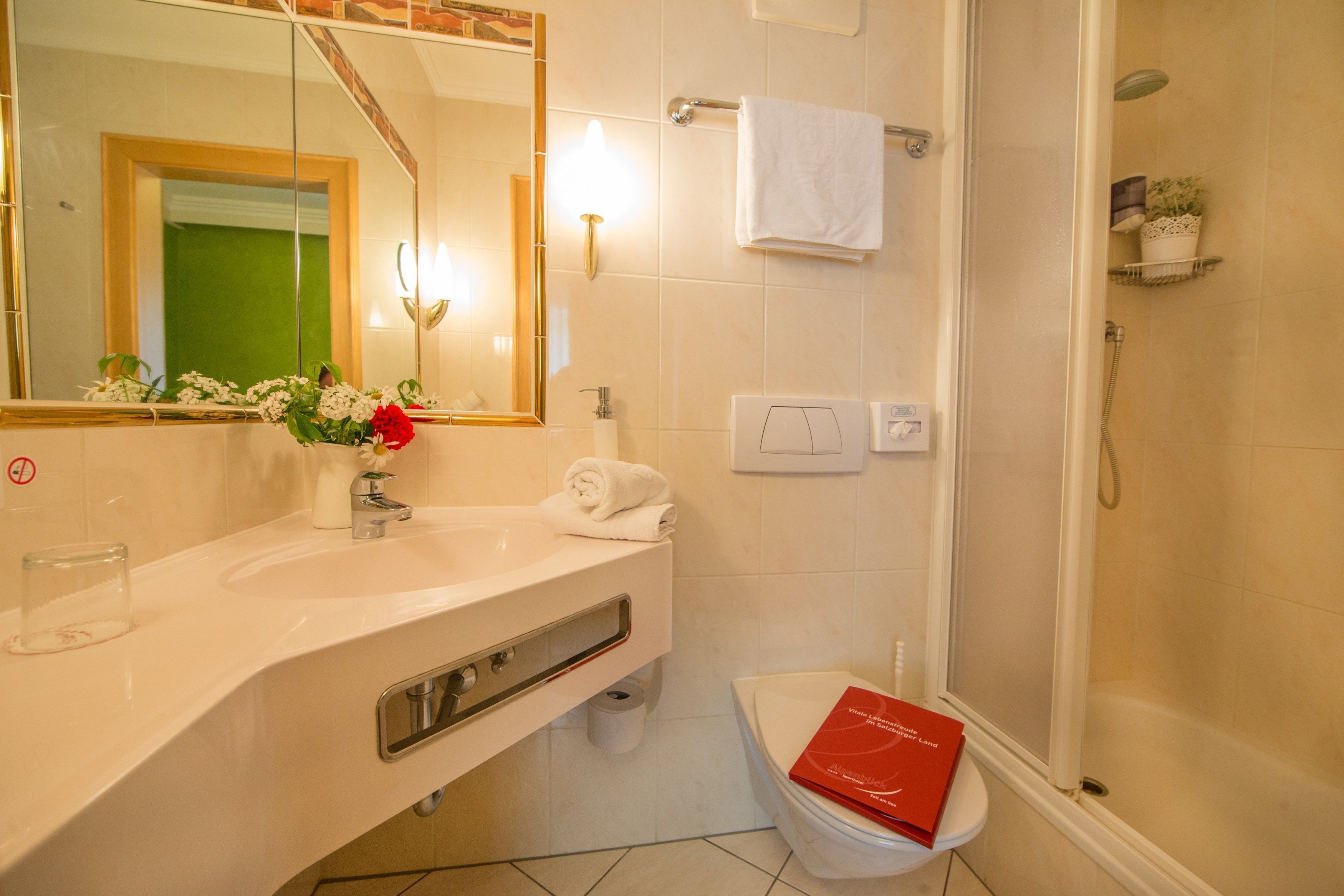 A bathroom with a white sink, mirror, and toilet. There is a shower curtain, a towel, and a book on the toilet.