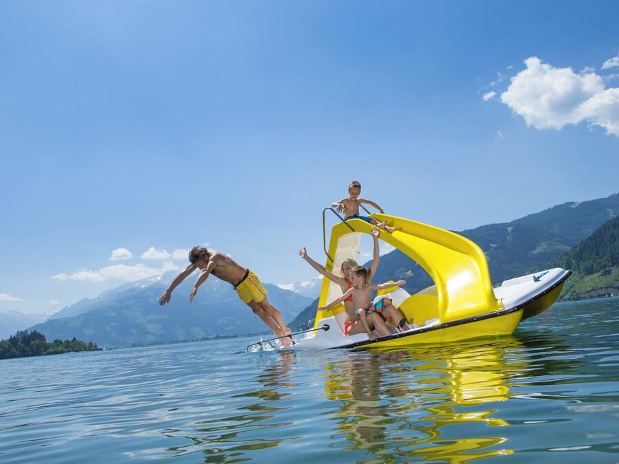 A boat with a yellow and white design on a lake with mountains in the background.