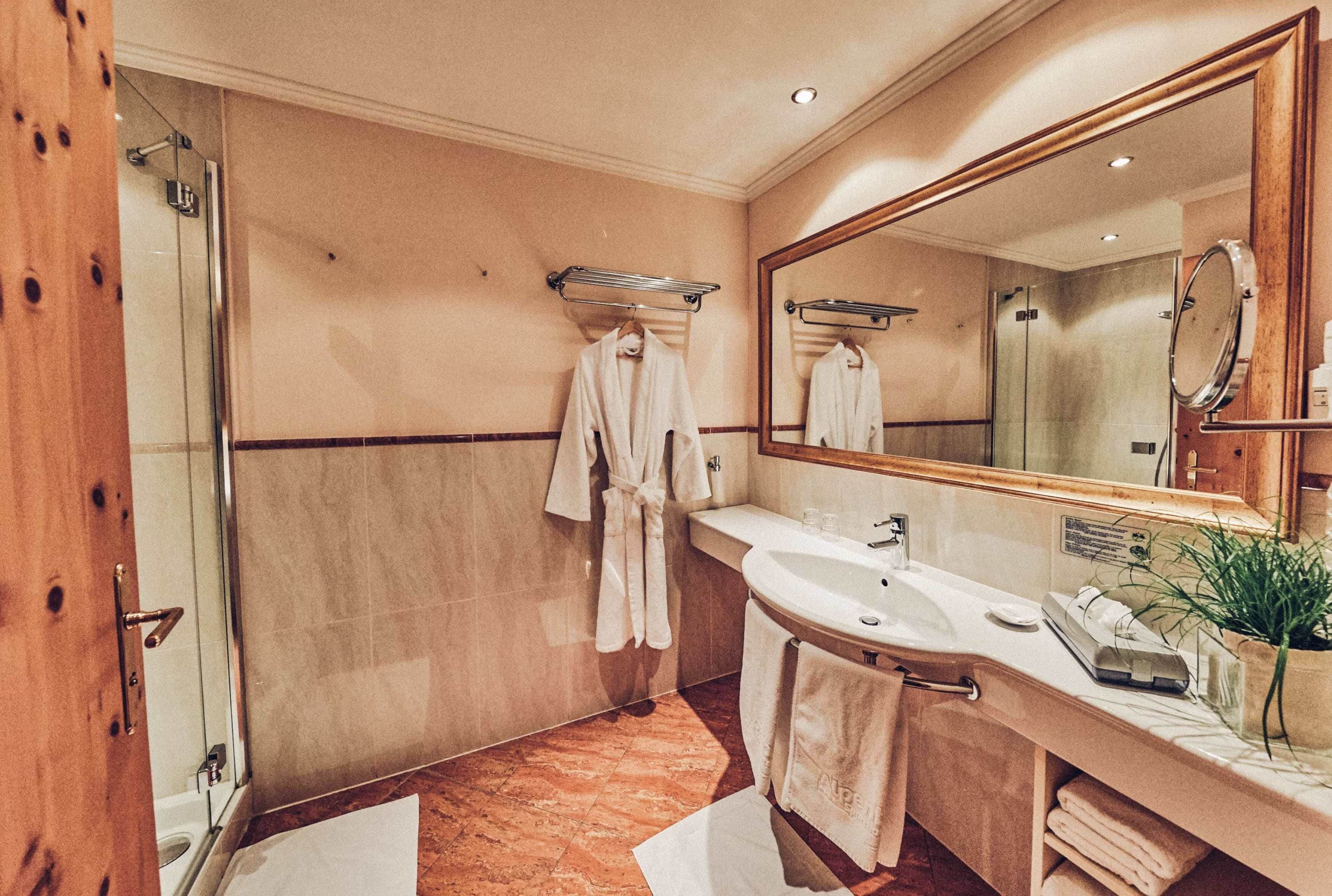 Un baño de hotel con ducha de vidrio, lavamanos, espejo y toallero.