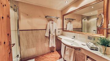 Un baño de hotel con ducha de vidrio, lavamanos, espejo y toallero.