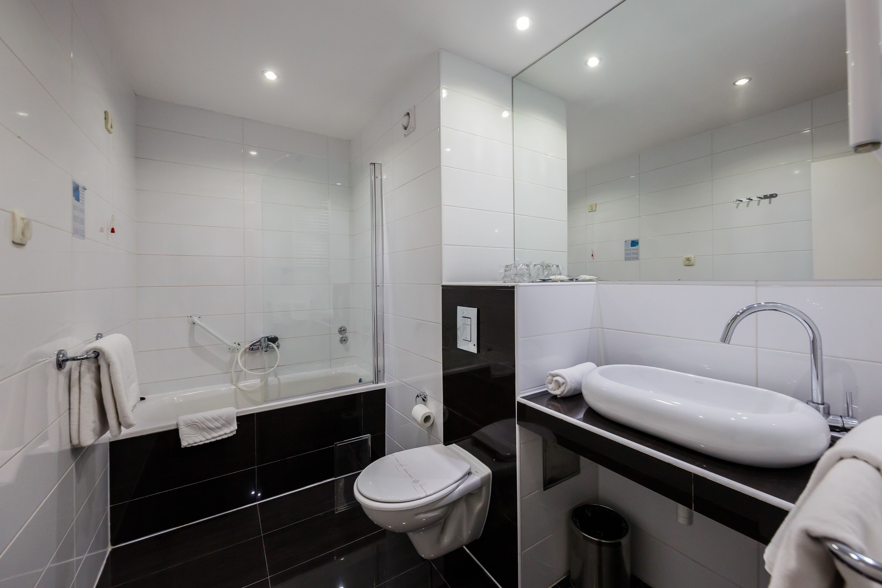 Een moderne badkamer met een badkuip, toilet, wastafel en een grote spiegel.