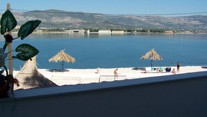 Una playa con sombrillas y sillas de descanso, vista despejada al agua y montañas al fondo.