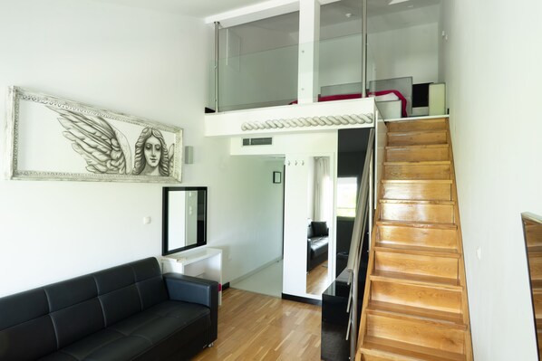 A modern interior with a black leather sofa, a staircase, and a framed artwork on the wall.