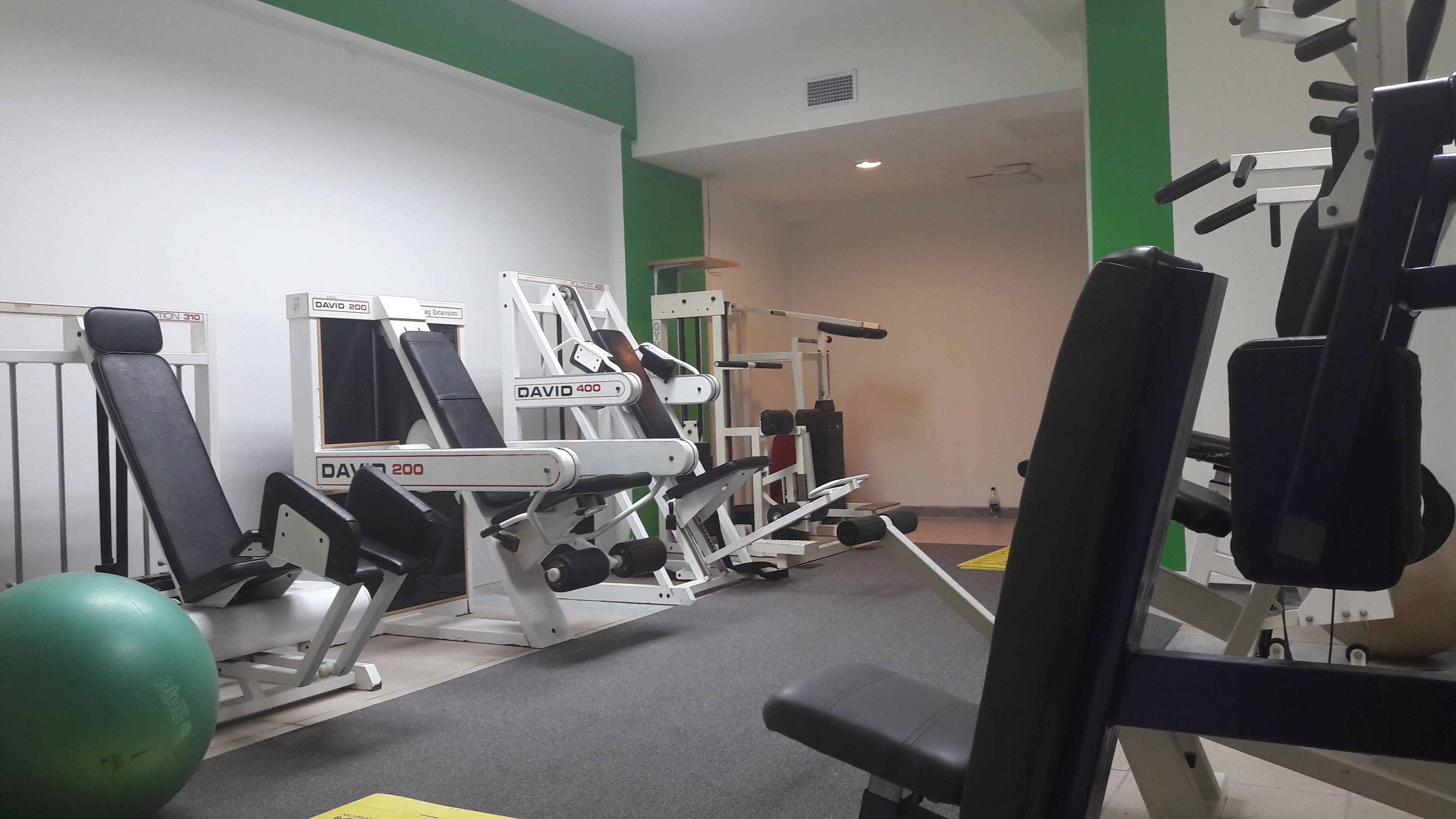 A gym with various exercise machines, a green exercise ball, and a bench.