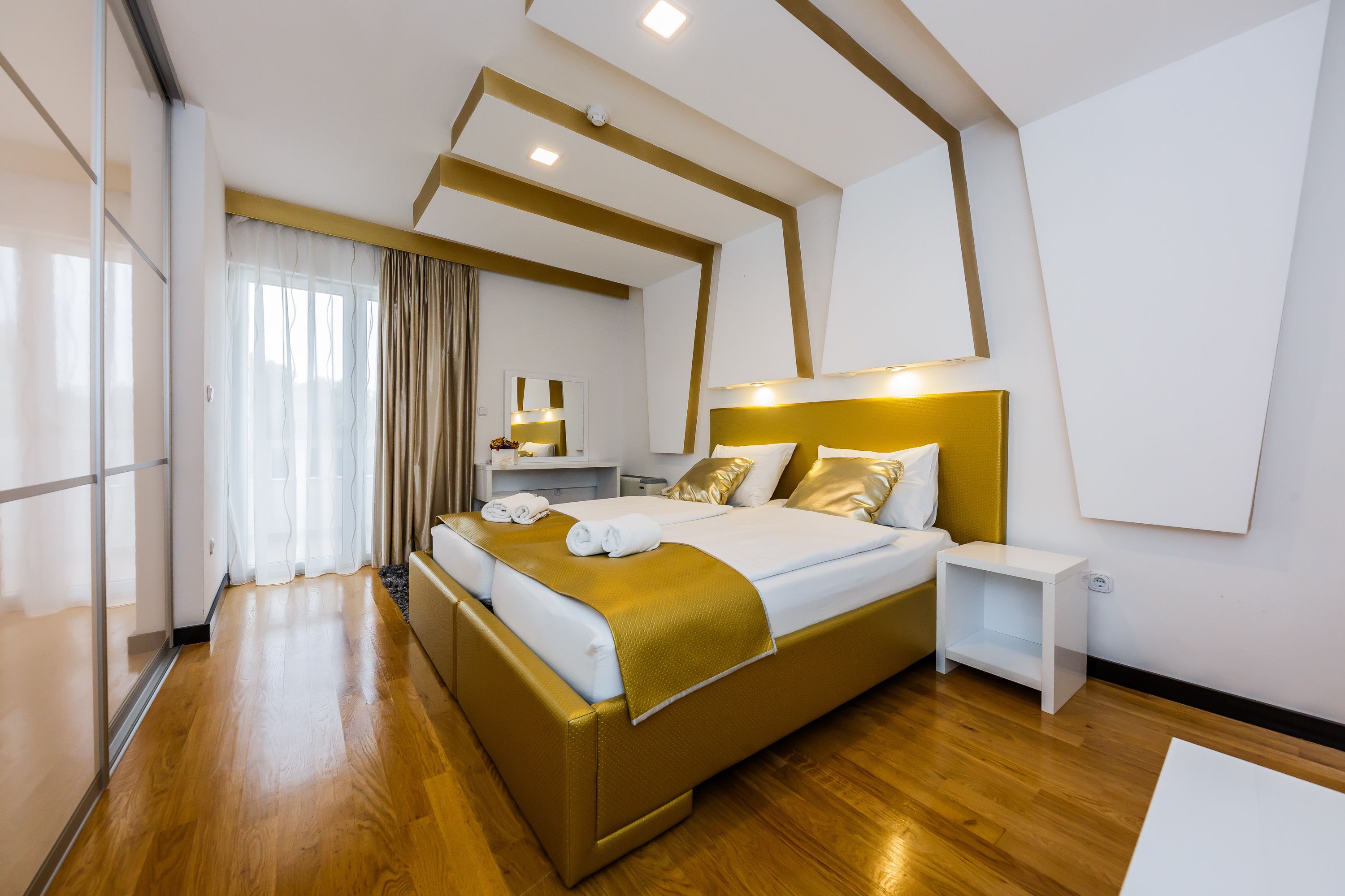 A modern hotel room with a large bed, a bedside table, a mirror, and a view of the city.