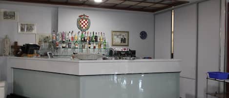 Eine Bar mit einer Theke, verschiedenen Flaschen, Gläsern und einem gerahmten Bild an der Wand.