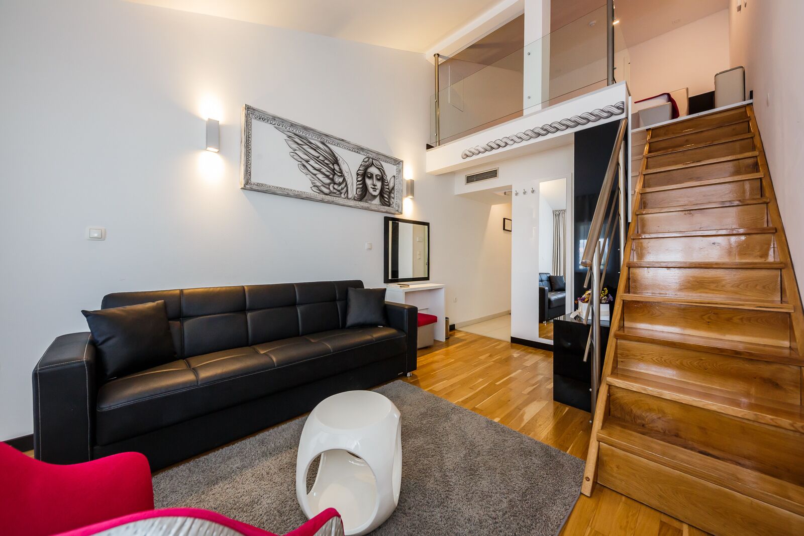 Un salon moderne avec un canapé en cuir noir, un coussin pour animal de compagnie blanc et un escalier en bois.