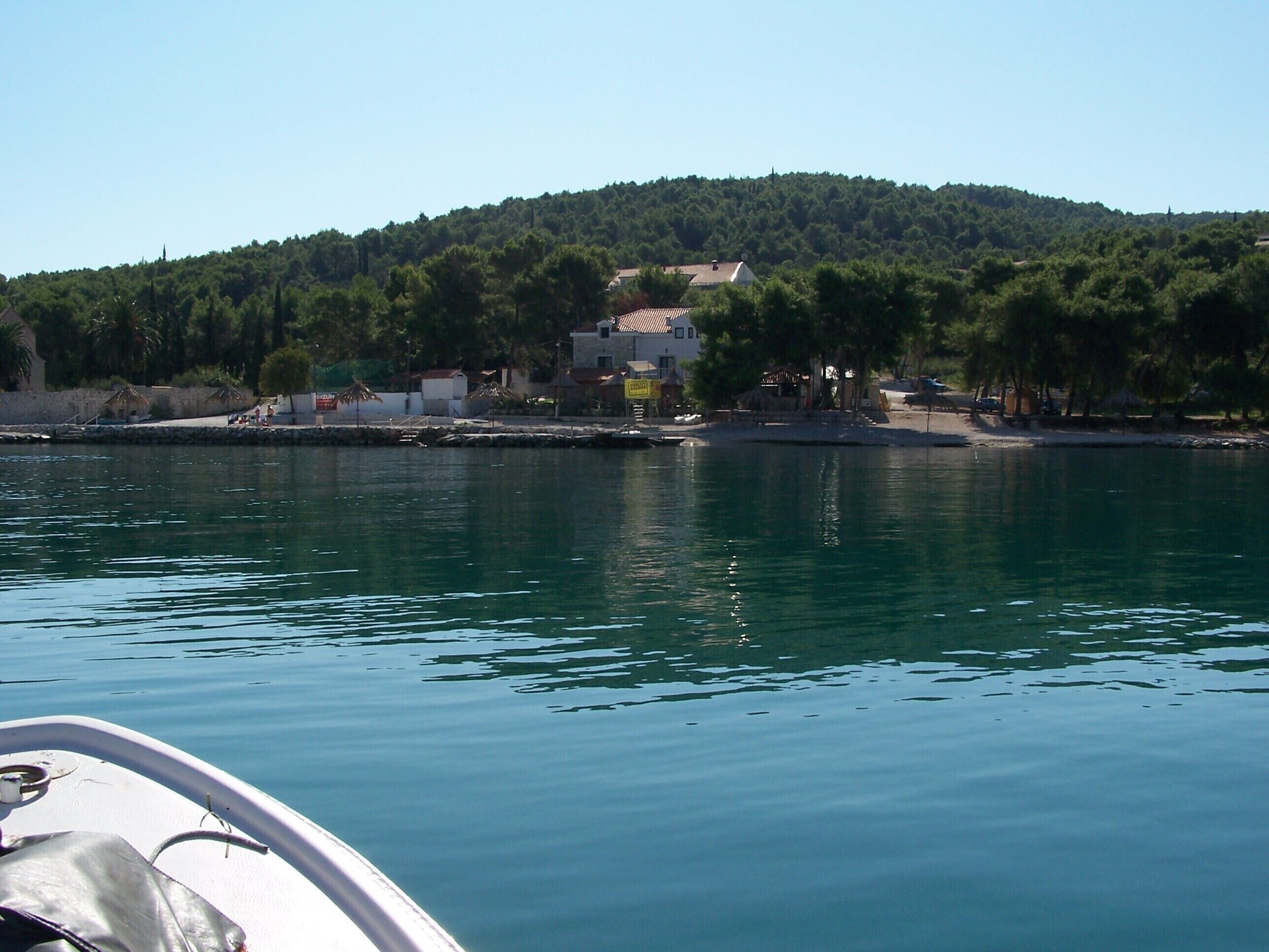 A coastal view with a boat in the foreground, a sandy beach, and a hill with buildings in the background.