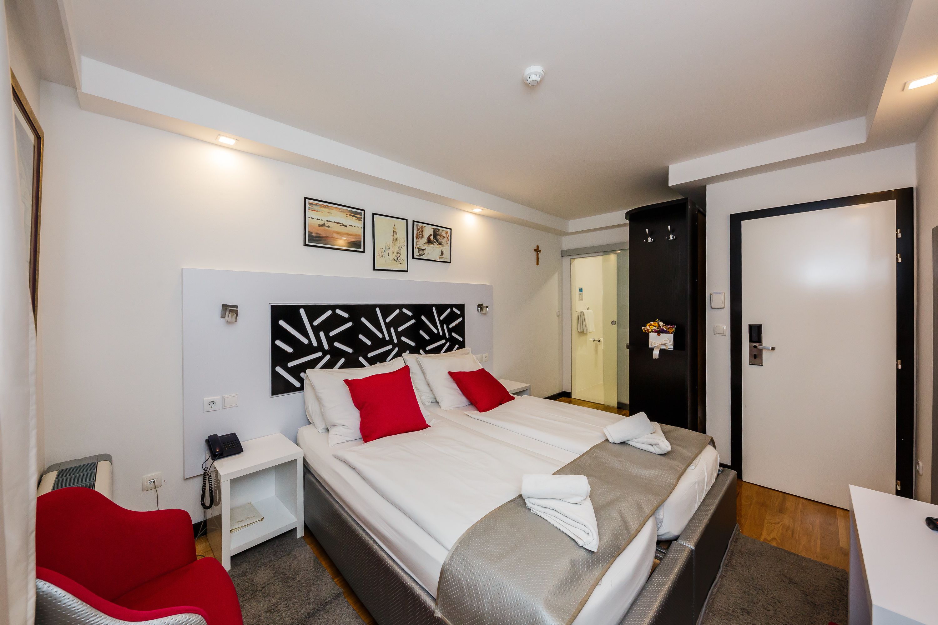 Une chambre d’hôtel moderne avec un grand lit, une table de chevet avec un téléphone, un fauteuil rouge et un bureau avec un ordinateur.