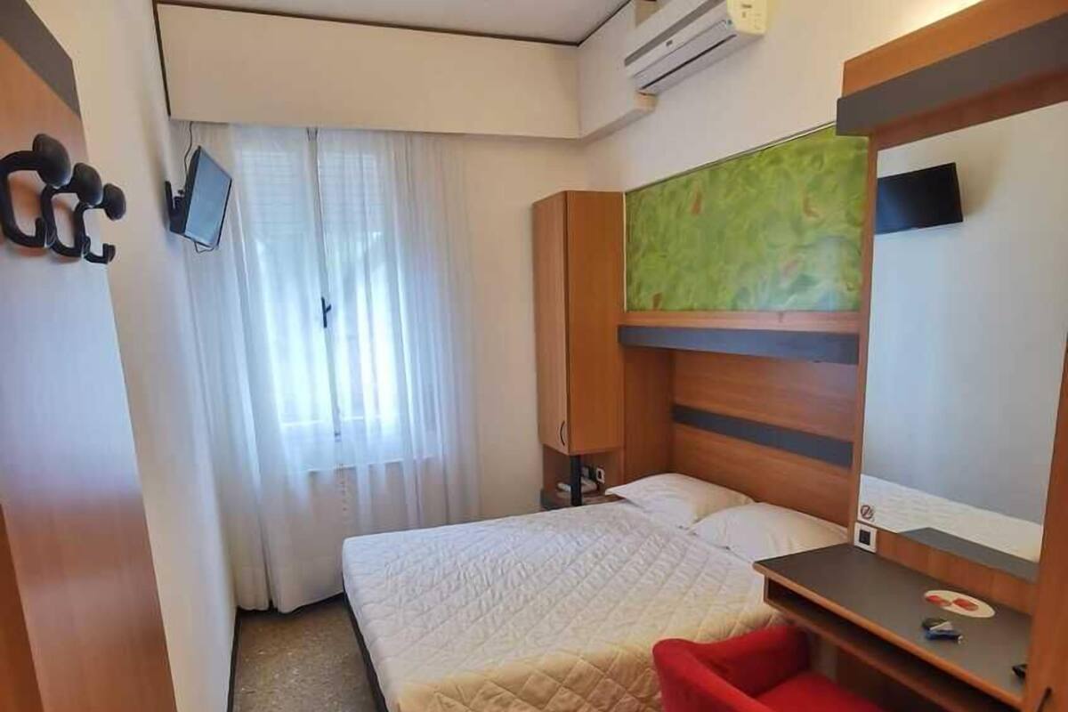 A compact hotel room with a bed, a desk, a red chair, and a ceiling fan.