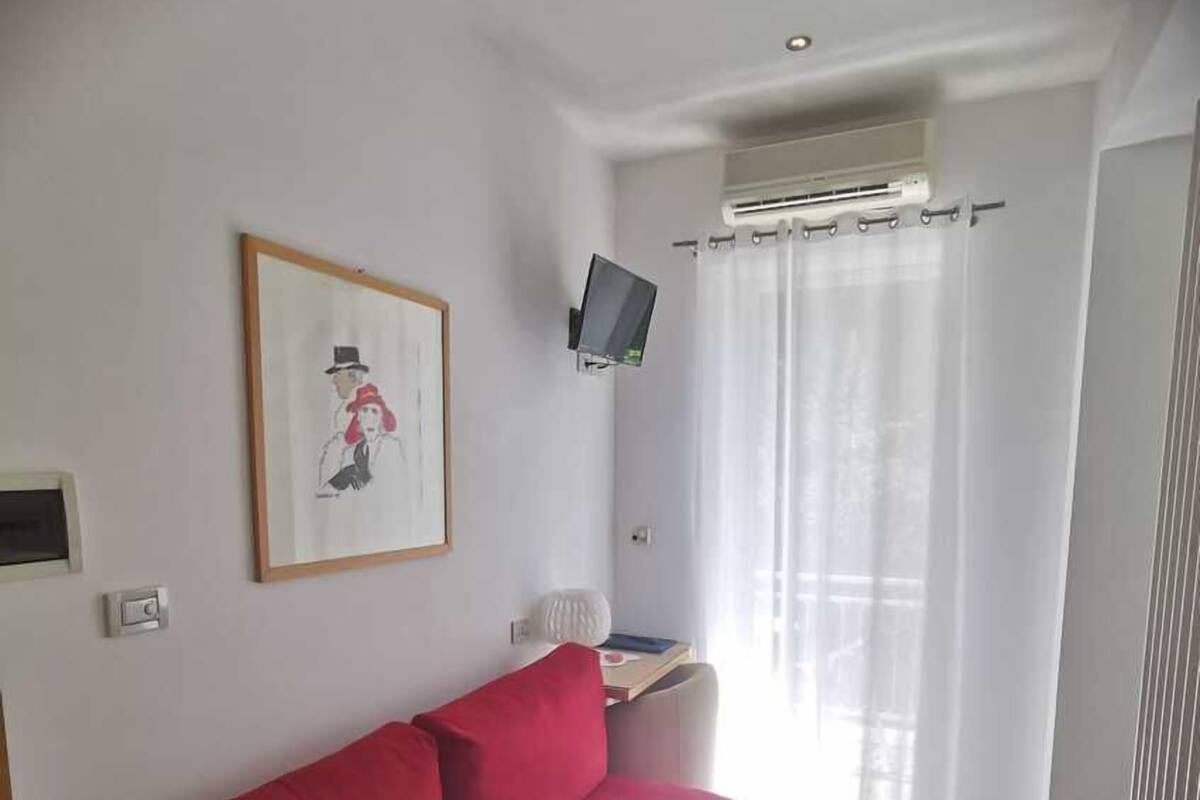 A room with a red sofa, a flat-screen TV mounted on the wall, and a window with curtains.