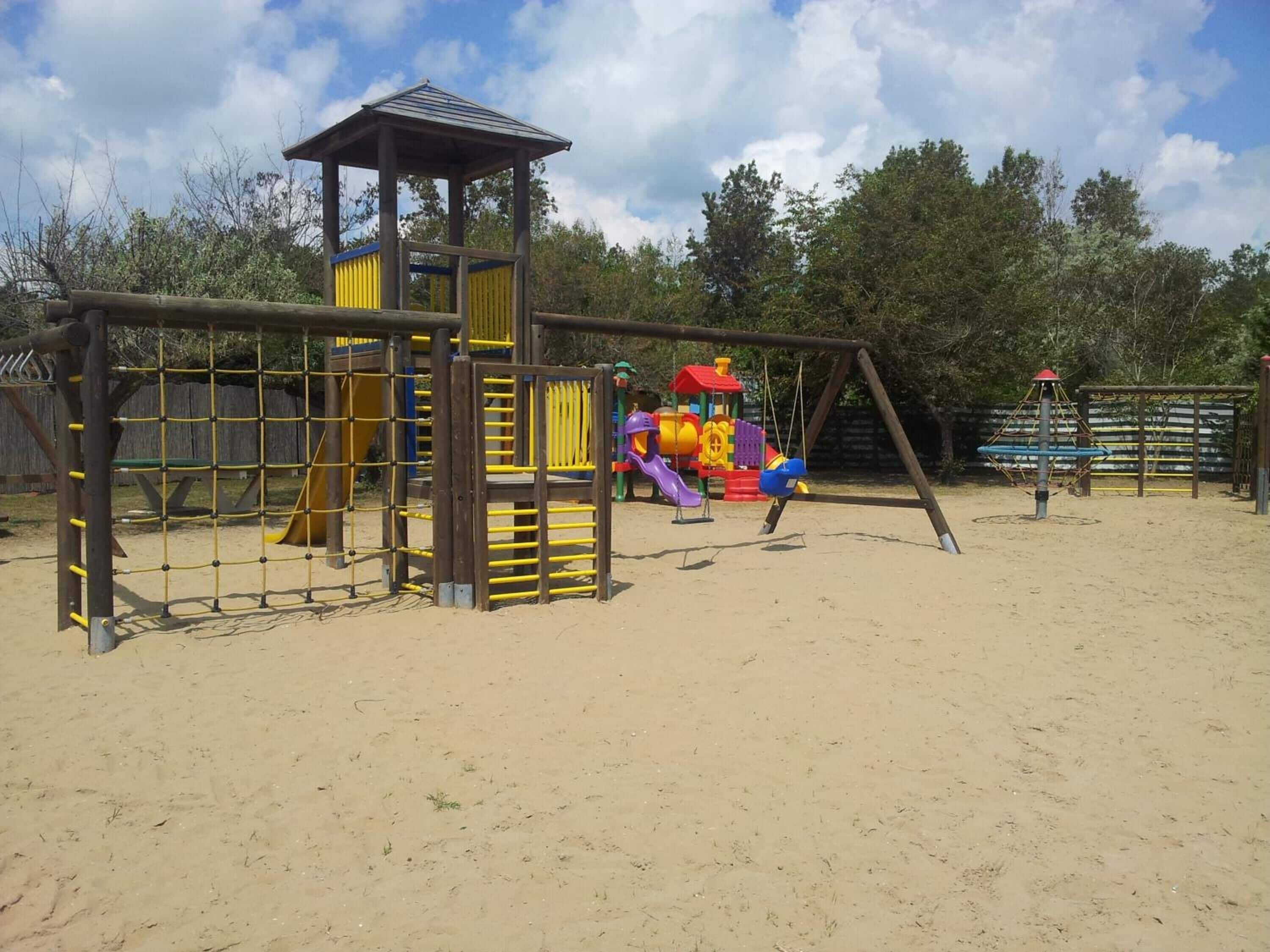 Un parque infantil con un elemento de escalada, columpios y un tobogán.