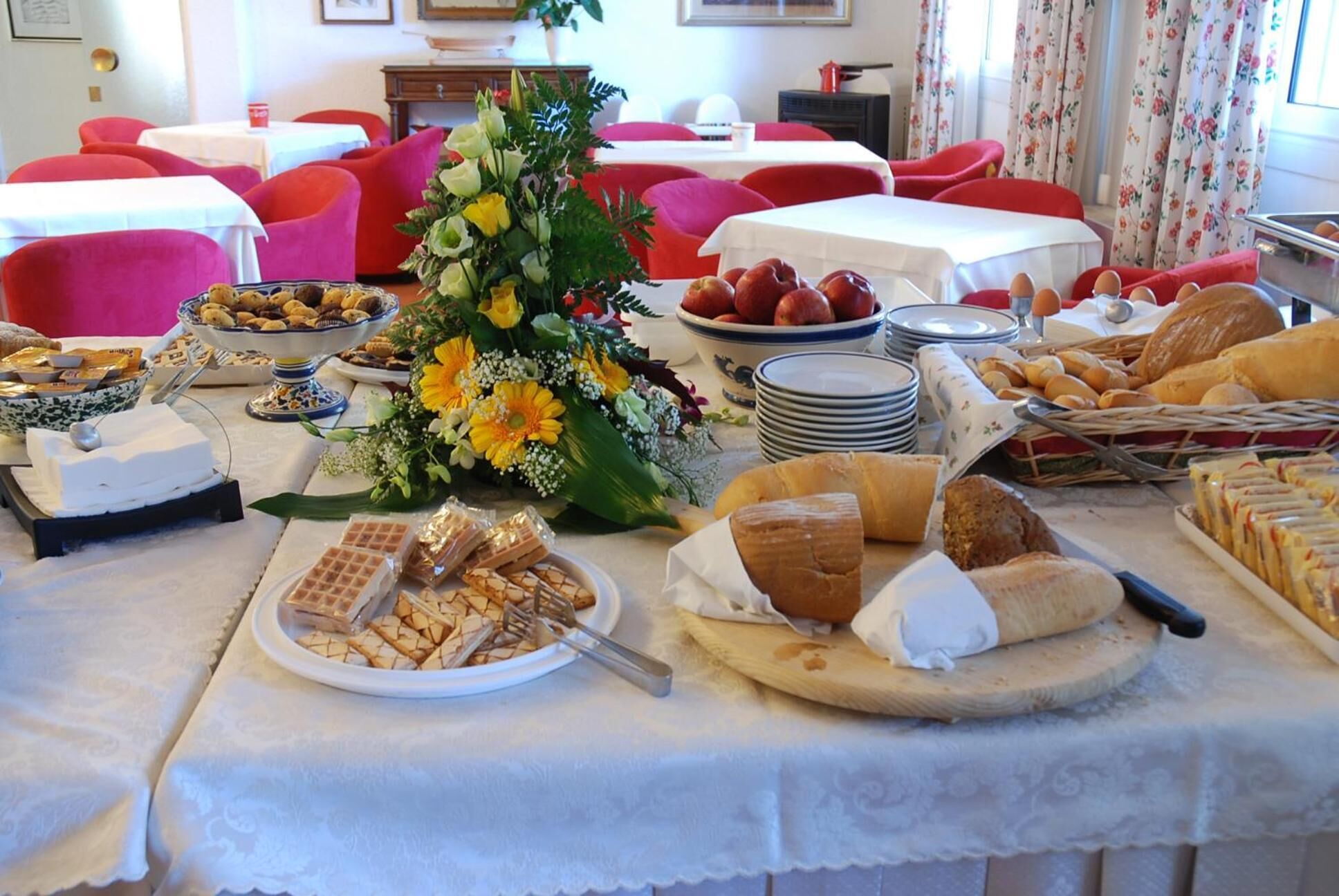 En buffetbod med forskellige spiser, herunder brød, kager og en blomsterdekoration.